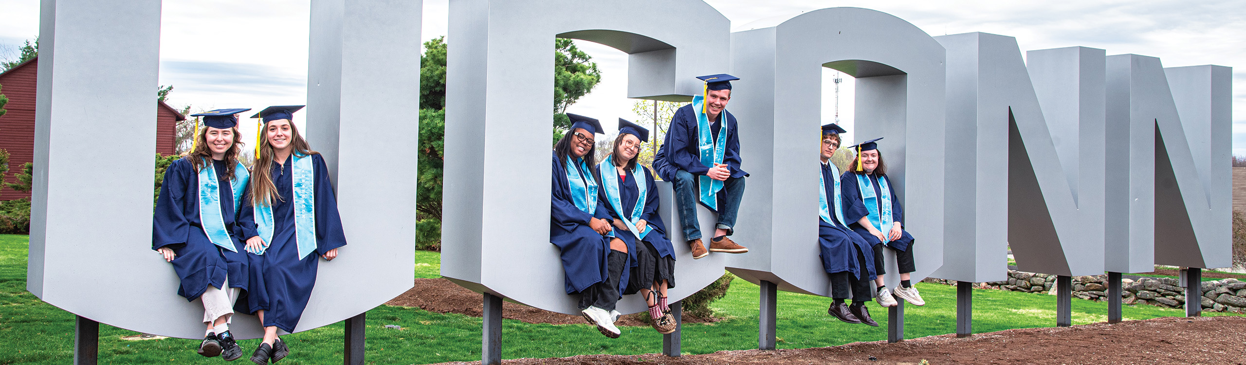 graduating students sitting on UConn sign